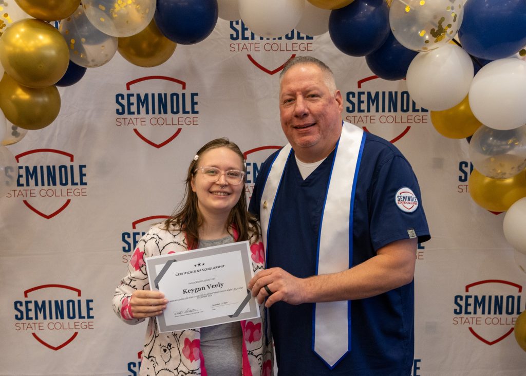 In this photo, Dusten Lancaster (right), president of Seminole State College's Fall 2024 nursing cohort, presents a $500 scholarship to fellow nursing student Keygan Veely (left). The graduating class raised the funds to support the scholarship effort.