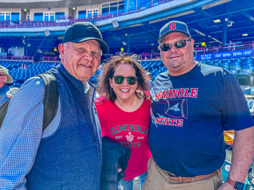 Posing for a photo, pictured (left to right): Former SSC Trojan Baseball Head Coach Lloyd Simmons, Pam Morgan, and former SSC Trojan catcher and current Chair of the SSC Board of Regents Curtis Morgan gather at Chickasaw Bricktown Ballpark to celebrate the Battle at Bricktown matchup between Seminole State and Rose State.